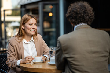 Businesswoman smiling and drinking coffee at outdoor cafe with colleague