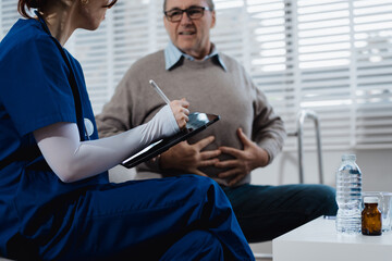 A young Caucasian nurse provides medical consultation to an elderly Caucasian man sitting on a...