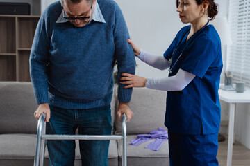 A white female nurse is assisting an elderly male patient with crutches, helping him get up from a...