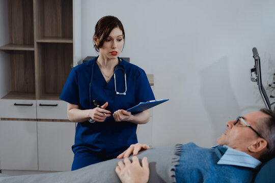 A white female nurse carefully takes notes while consulting an elderly male patient lying in bed, focusing on health care monitoring, medical assessment, nursing care, and patient support - Powered by Adobe