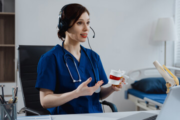 A young nurse wearing a headset conducts an online medical consultation, holding a joint model to explain musculoskeletal conditions,focusing on bone joint health, patient education, orthopedic care