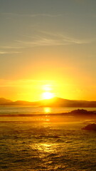 A breathtaking view of a golden sunset over the sea, featuring a silhouette of a lighthouse and distant mountains. The sun’s rays reflect on the water’s surface, creating a warm and radiant atmosphere
