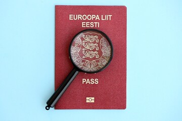 Estonia passport and magnifying glass on light blue paper. Citizenship details and information