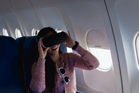 Asian businesswoman wearing VR headset while sitting on an airplane.Immersed in virtual reality entertainment,exploring technology,enjoying a futuristic immersive travel experience during her flight - Powered by Adobe