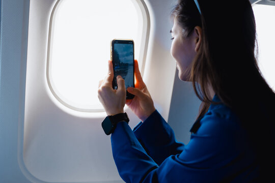 A cute Asian woman enjoys a fun travel experience on a plane, smiling happily while sitting by the window, reflecting the relaxation, freedom and excitement of her travel during the trip