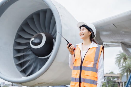 An Asian woman stands confidently in front of a jet engine,wearing a safety helmet  reflective vest,holding tablet,representing aviation engineering,safety inspection,professional roles in airline