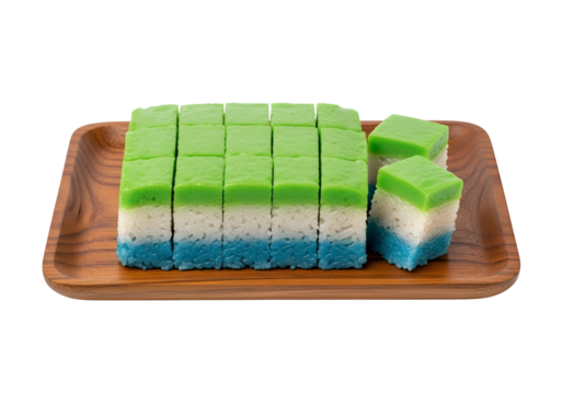 A wooden tray holds colorful, cubed rice cakes, showcasing vibrant green, white, and blue layers.
