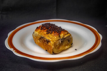 Bolen pastry with golden crust and dark filling topped with chocolate sprinkles on ceramic plate highlighting rich layers, baked texture, and sweet appeal for food styling and dessert branding.