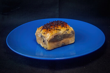 Indonesian bolen pastry with glossy crust, dark fill, and chocolate sprinkles on blue plate highlighting rich layers, sweet texture, and artisanal dessert appeal for culinary content.
