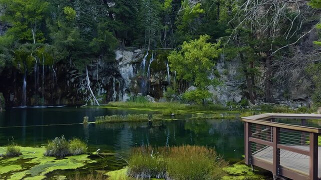 Still surface of Hanging Lake mirrors surrounding trees and canyon walls in soft light, empty observation deck