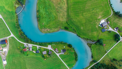 Nestled in Stryn, Norway, lush green fields frame the winding turquoise river under clear skies....