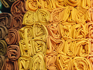 A stack of colorful hijabs or headscarves neatly folded into a square roll. A head covering for Muslim women.