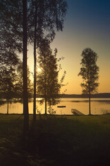 Romantic sunset on the lake with boat, jetty and forest silhouettes