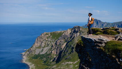 A solitary hiker stands at the edge of Matind Mountain, taking in the breathtaking coastal views of...