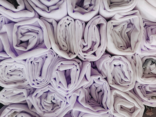 A stack of colorful hijabs or headscarves neatly folded into a square roll. A head covering for...