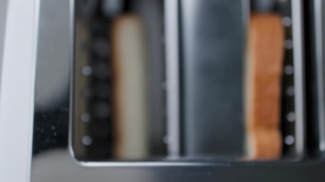 Close-up of two slices of bread toasting in a metallic, two-slot toaster.  The bread is browning, and the toaster's sleek surface reflects light