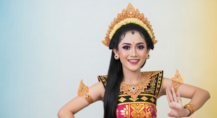 A beautiful young Balinese woman in traditional costume and ornate headdress smiling while performing a cultural dance.