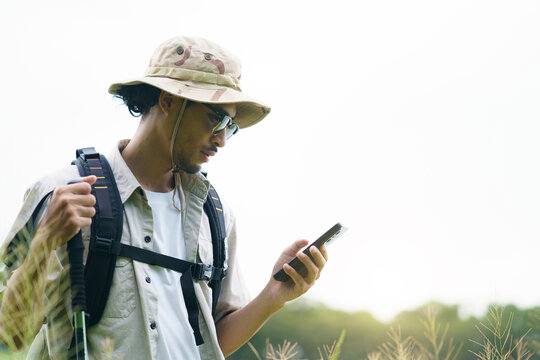 Asian male hiker with backpack looking at smartphone map while trekking outdoors in nature.