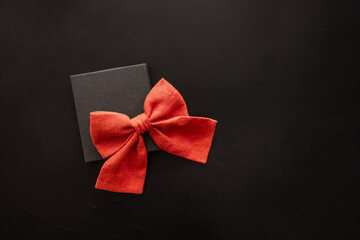 A black gift box with a large red bow on a dark background. The scene conveys a festive atmosphere suitable for Black Friday sales.