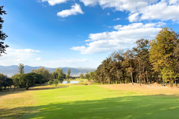 Beautiful golf course view with mountains, forest, and bright sky, showing a scenic fairway and sand bunker.