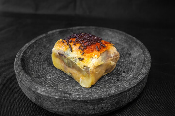 Golden baked pastry slice with flaky crust and savory filling, topped with chocolate sprinkles on dark plate ideal for highlighting texture, fusion topping, and snack appeal.