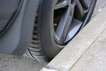 Car tire closeup touching curb edge, risk of sidewall damage, rim scraping, and parking hazard. Wheel rim close to concrete surface, risk of tire wear, scratches, and costly repairs. Selective focus