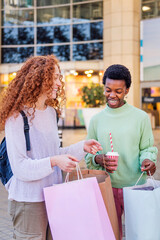 two young women in front of mall looking inside of shopping bag, concept of friendship and urban lifestyle