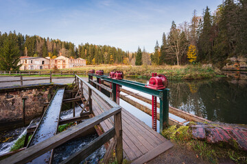 An old abandoned water mill and a historic dam with a red sluice gate mechanism on the river in a...