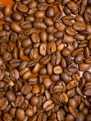 Roasted coffee beans scattered on brown background closeup