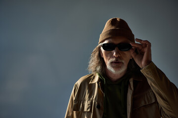 Senior man exudes confidence in stylish outfit and trendy sunglasses under soft lighting