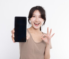 Fototapeta premium Asian young woman showing or presenting mobile phone application and ok sign isolated over white background