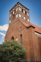 A tall brick building with a red roof and a green tree in front of it