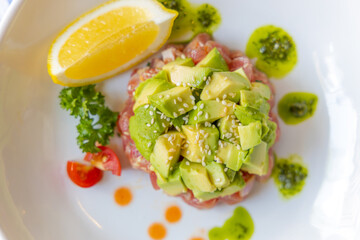 Delectable Avocado Tuna Tartare: A gourmet tuna tartare is artfully arranged, crowned with diced avocado, a wedge of lemon, and artful drizzles of sauce, offering a visual and culinary delight.