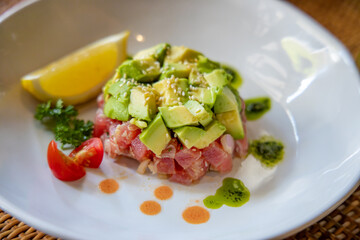 Delectable Avocado and Tuna Tower: A mouthwatering dish featuring a precisely arranged avocado and tuna tower, garnished with fresh herbs, a juicy lemon wedge, and artistic drizzles.