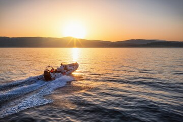 Aerial view of a sports RIB boat cruising with speed over the calm ocean during summer sunset time