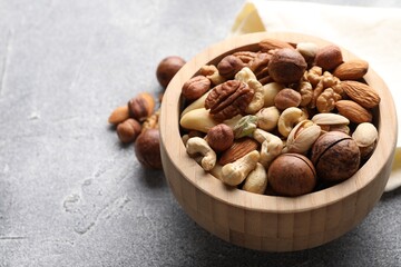 Mix of different nuts in bowl on grey textured table, closeup. Space for text