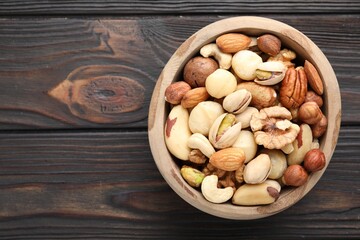 Mix of different nuts in bowl on wooden table, top view. Space for text