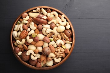Mix of different nuts in bowl on black wooden table, top view. Space for text