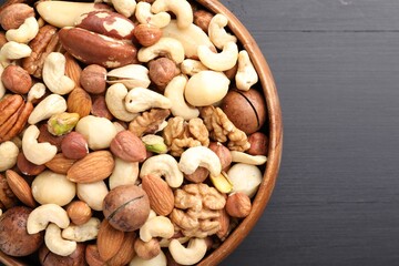 Mix of different nuts in bowl on black wooden table, top view. Space for text