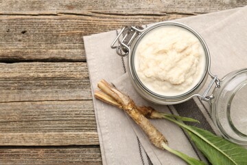Tasty horseradish sauce and roots on wooden table, flat lay. Space for text