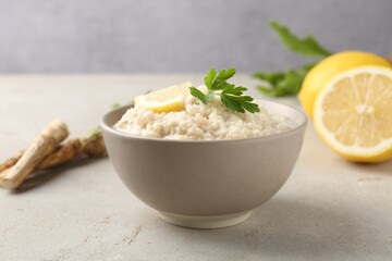 Tasty horseradish sauce with parsley, lemon slice and roots on light table, closeup