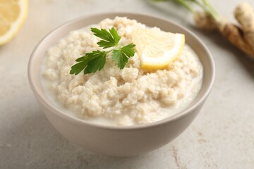 Tasty horseradish sauce with parsley and lemon slice on light table, closeup