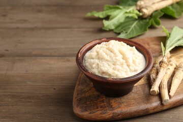 Tasty horseradish sauce and roots on wooden table, closeup. Space for text