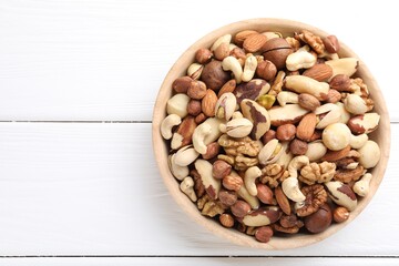 Mix of different nuts in bowl on white wooden table, top view. Space for text