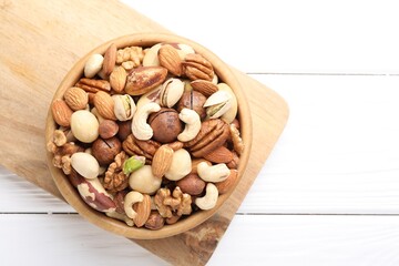 Mix of different nuts in bowl on white wooden table, top view. Space for text