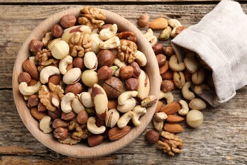 Mix of different nuts in bowl and bag on wooden table, top view
