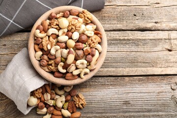 Mix of different nuts in bowl and bag on wooden table, top view. Space for text