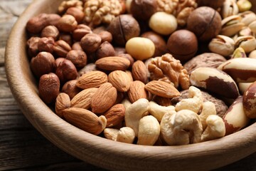 Mix of different nuts in bowl on wooden table, closeup