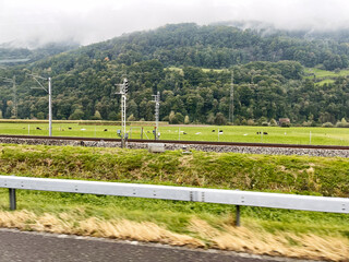 Fototapeta premium Peaceful Swiss countryside with green fields, mountains, and railway infrastructure