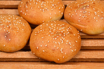 close-up shot of four fresh, golden-brown sesame seed buns on a rustic, grooved wooden breadboard